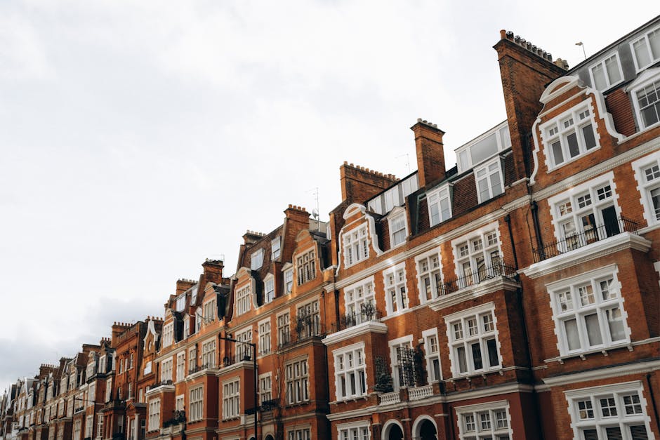 A row of historic red-brick residential buildings along Fulham Road, featuring white window frames and decorative brickwork, with black metal balconies and chimney stacks visible atop the structures. The buildings are illuminated by natural daylight under an overcast sky, highlighting the architectural detail and maintaining a clean, well-preserved appearance. This image represents an exterior view of typical Fulham flats, aligning with the Fulham Road flat cleaning guide for residents by Cleaner Fulham, emphasizing the importance of surface maintenance and exterior hygiene in residential settings.